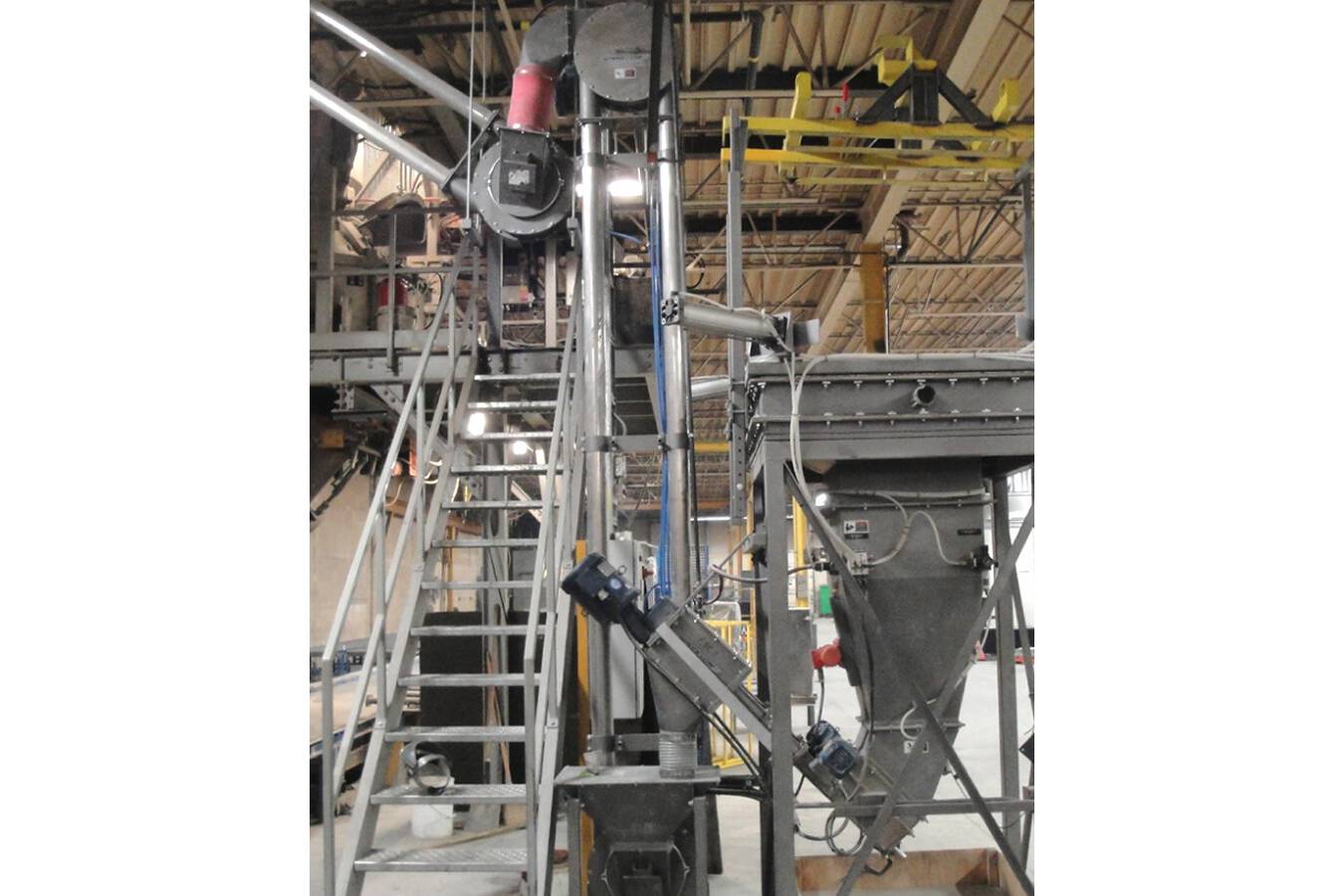 Ein vertikaler mechanischer Aero-Förderer befördert das Zementpulver von zwei flexiblen Schneckenförderern zu einem zweiten mechanischen Aero-Förderer, der durch das Gebäudedach zu einem Lagersilo im Freien führt.